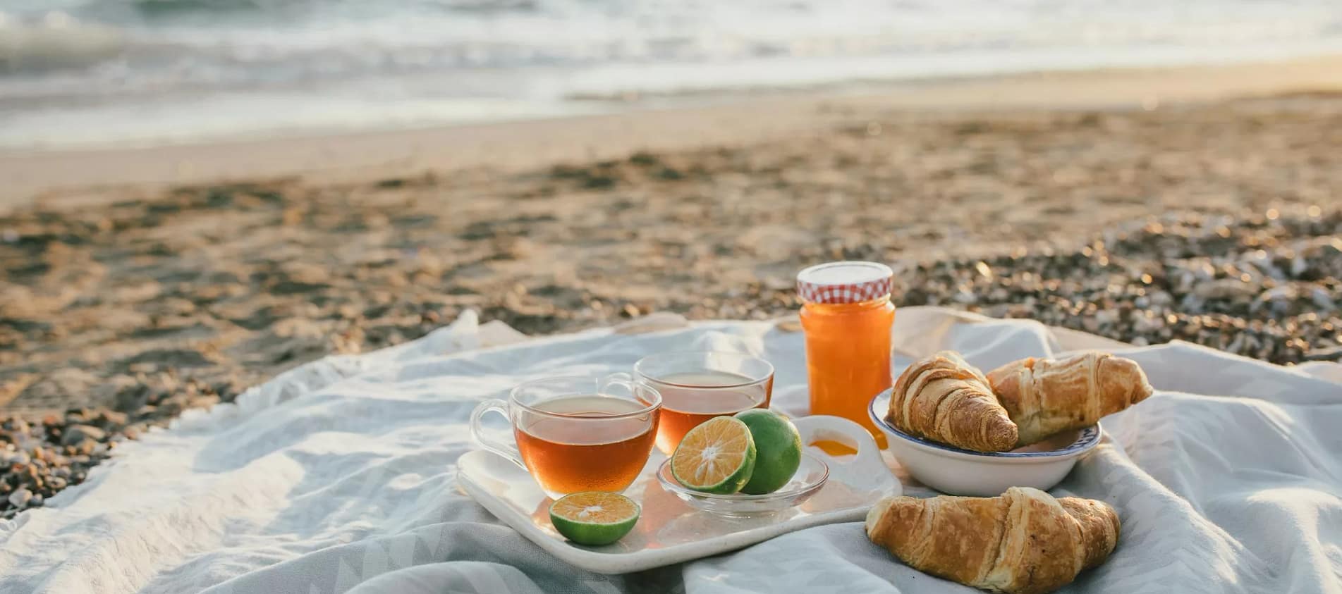 Tasty summer picnic with fresh tea and croissants on the beach at sunset.