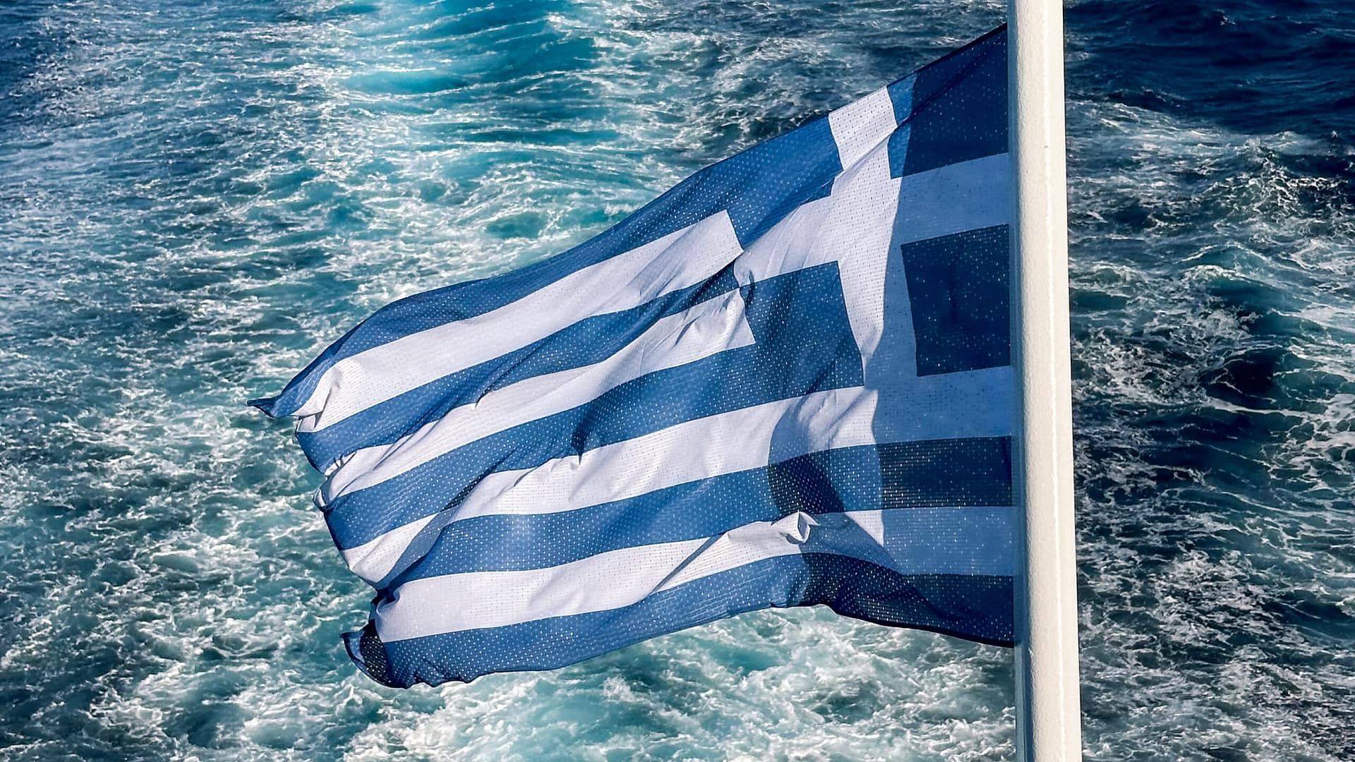 The wake of the water behind the ferry with Greek Flag